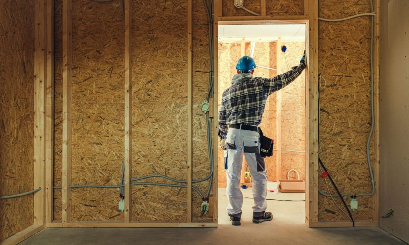Construction worker leaning against door frame of interior room in house being built.